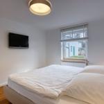Schlafzimmer mit Bett, Fenster und Wandfernseher.