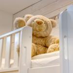 Ein weißes Kinderbett mit einem großen Teddybären darauf.