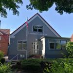 Landhaus am Ufer mit grauer Fassade und rotem Dach unter blauem Himmel.