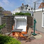 Terrasse mit Strandkorb, Holzstühlen und Brunnen. Hintergrund: Holzzaun und Gebäude.