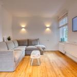 Wohnzimmer mit grauem Sofa, Holzboden und Wandfernseher.