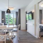 Wohnbereich mit Esstisch, Sofa und TV. Schlafzimmer mit Bett und Fenster sichtbar.