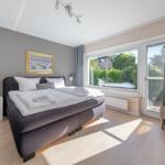 Schlafzimmer mit Doppelbett, Fenster und Gardinen.