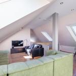 Dachgeschosswohnung mit grünem Sofa, Fernseher und Dachfenstern.