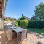 Terrasse mit Tisch, Stühlen und Pavillon. Grünflächen und Hecke im Hintergrund.