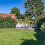 Hinterhof mit Terrasse, Liegestühlen und Hängematten umgeben von Grünflächen und Bäumen.