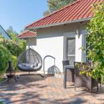 Terrasse mit Hängesessel, Tisch und Stühlen, umgeben von Grün und einem Haus mit rotem Dach.