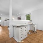 Helle Arbeitsfläche mit Stuhl und Schubladen. Im Hintergrund TV und Schlafzimmer.