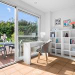 Helle Arbeitszimmer mit Schreibtisch, Bücherregal und Terrasse mit Gartenblick.