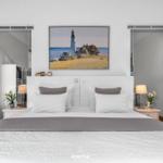 Schlafzimmer mit Bett, Nachttischen und Wandbild mit Leuchtturm.