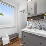 Badezimmer mit Waschtisch, Spiegelschrank und Fenster mit Blick auf Außenbereich.