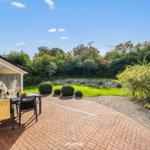 Terrasse mit Tisch und Stühlen, grüner Garten und Steinmauer im Hintergrund.