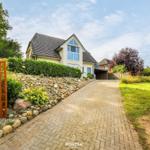 Haus mit gepflasterter Straße, Rasen und Steinmauer. Schild mit Ferienwohnung.