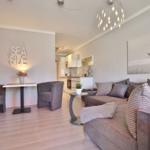 Wohnzimmer mit Sofa, zwei Sesseln und Küchenbereich im Hintergrund.