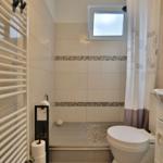 Badezimmer mit Dusche, Toilette und Waschbecken. Fliesen und Duschvorhang sichtbar.