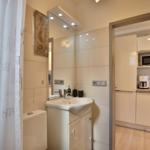 Badezimmer mit Waschbecken, Spiegel und Dusche. Küche mit Mikrowelle und Kaffeemaschine sichtbar.