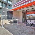 Terrasse mit Sitzgruppe, Tisch, Stuhl und orangefarbenem Markisenüberdachung.