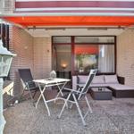 Terrasse mit orangefarbenem Markisenüberdachung, Tisch, zwei Stühle und Sofa. Boden aus Kies.