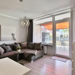 Wohnzimmer mit Sofa, Glasfront und Balkon mit Sonnenschutz.