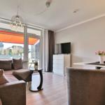 Wohnzimmer mit Sofa, Esstisch und TV. Durchgang zur Terrasse mit orangefarbenem Sonnenschutz.