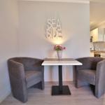 Essbereich mit zwei Sesseln und Tisch. Küchenbereich im Hintergrund.