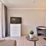 Wohnzimmer mit TV, Schreibtisch und Sitzgelegenheiten. Fenster zur Terrasse.