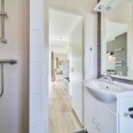 Bad mit Dusche, Waschbecken und Spiegel. Blick in Wohnbereich.