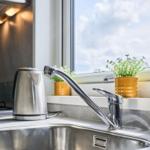 Küchenzeile mit Wasserhahn, Kanne und Pflanze am Fenster