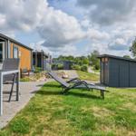 Terrasse mit Tisch und Stühlen, Liegestühle auf Rasen, Gartenhaus und Ferienhaus im Hintergrund.