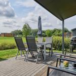 Terrasse mit Tisch, Stühlen und Grill. Blick auf Grasfläche und Bäume.