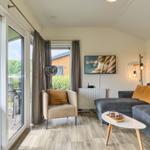 Wohnzimmer mit Sofa, Sessel und TV. Durchgang zur Terrasse mit Gartenansicht.