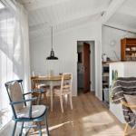 Kitchen and dining area with wooden floor and white walls. A window with curtain and chairs.