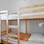 Room with two bunk beds, wooden frame, white dresser, and window with curtain.
