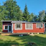 Rotes Holzhaus mit Terrasse und Fenstern, umgeben von Bäumen und Gras.