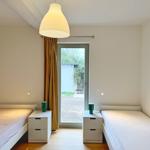 Zwei Einzelbetten mit Nachttischen und Lampen. Tür zum Außenbereich mit Vorhang.