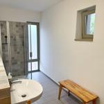 Bad mit Dusche, Waschbecken und Holzbank. Fenster mit Blick nach außen.