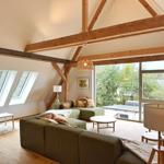 Wohnzimmer mit grünem Sofa, Holzbalken und großen Fenstern zur Außenterrasse.