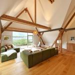 Großes Wohnzimmer mit grünen Sofas, Holzboden und Holzbalken an der Decke.