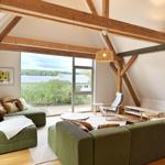 Wohnzimmer mit grünem Sofa, Holzbalken und großem Fensterblick.