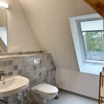 Badezimmer mit Dachfenster, Waschbecken und Toilette unter Holzbalken.