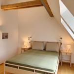 Schlafzimmer mit Dachschräge, Holzbalken und zwei Nachttischen mit Lampen.