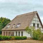 Haus mit Strohdach und Fachwerk, umgeben von Bäumen und Sträuchern.