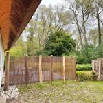 Hinter dem Haus befindet sich ein Garten mit Holzzaun und Tisch. Im Hintergrund sind Bäume zu sehen.