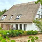 Haus mit Strohdach und Fenstern, umgeben von Grünflächen und Bäumen.