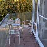 Terrasse mit Metalltisch und Stühlen, umgeben von Bäumen.