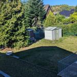 Grüner Garten mit Schuppen und Bänken. Hinterhof mit Zaun und Bäumen.