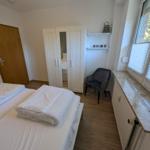 Schlafzimmer mit Bett, Kleiderschrank und Sitzgelegenheit neben Fenster.