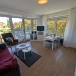 Wohn- und Essbereich mit Balkon, Holzboden und weißen Möbeln.