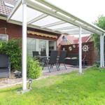 Terrasse mit Sitzgelegenheiten unter einem weißen Dach, umgeben von Grünflächen und einem Holzzaun.