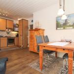 Essbereich mit Holztisch und Stühlen. Küchenbereich mit Holzmöbeln und Dunstabzug.